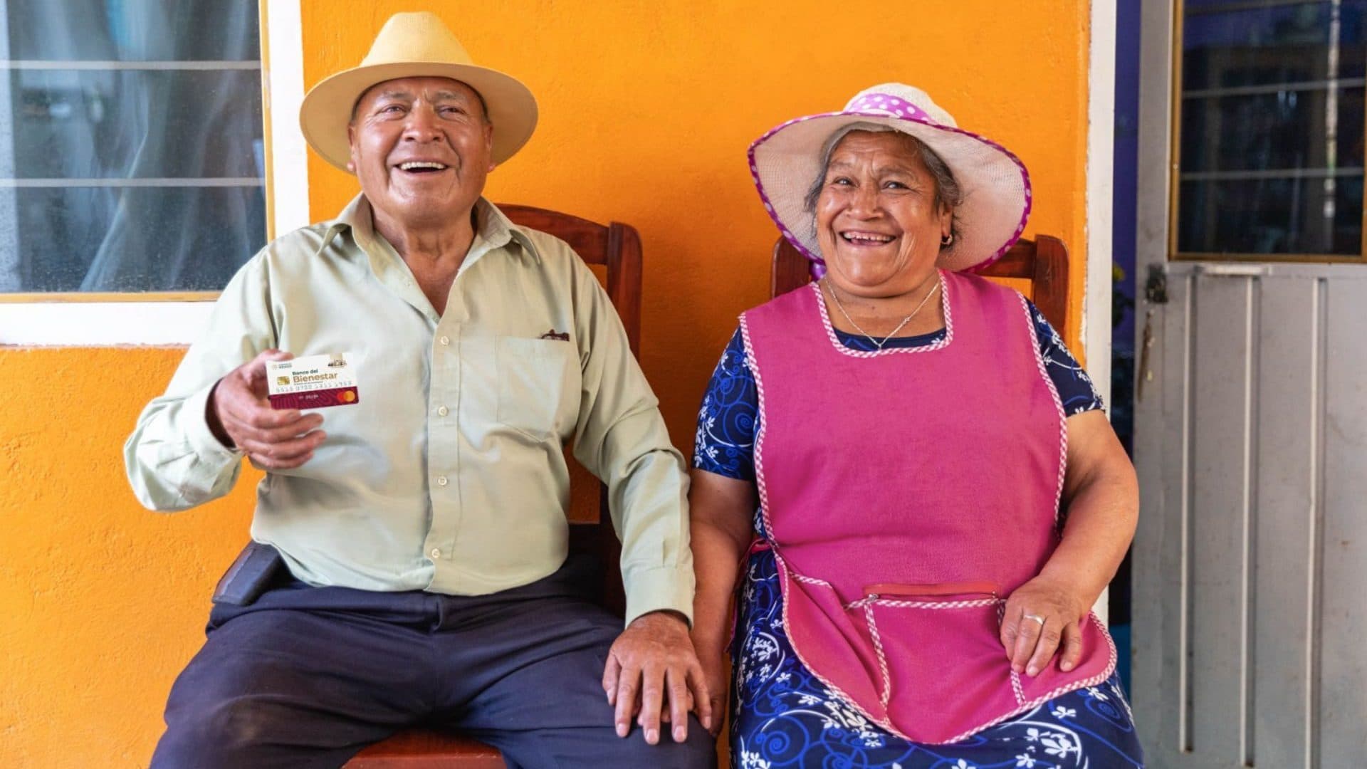 Una pareja de adultos mayores sostiene una tarjeta del Bienestar donde recibirán el pago de su Pensión Bienestar