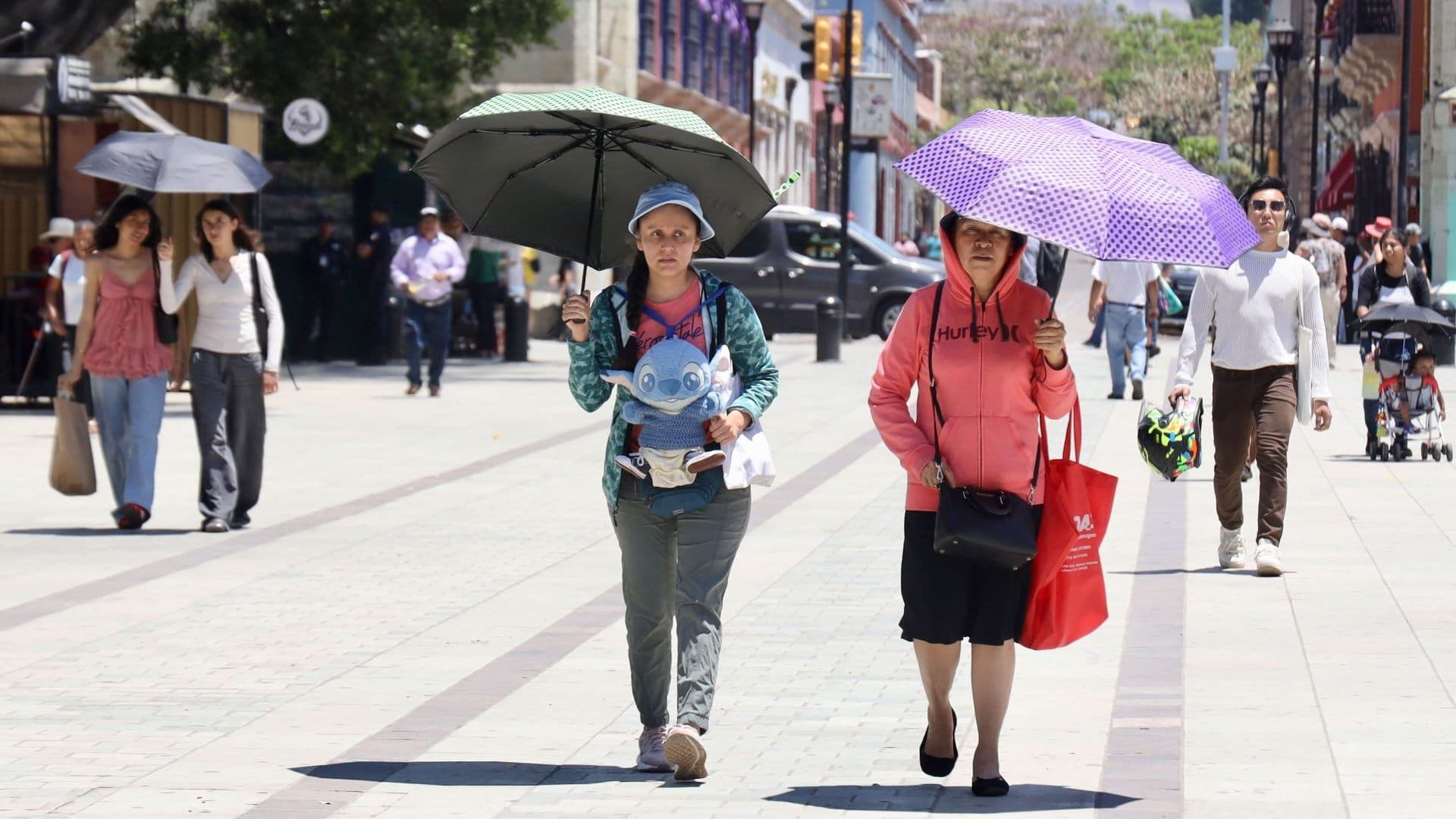 Dos mujeres caminan y usan sombrillas para protegerse del calor en Oaxaca